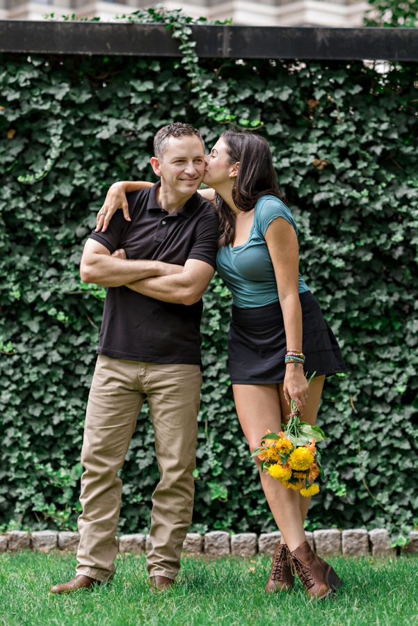 A newly engaged couple kiss in front of an ivy wall in Philadelphia.
